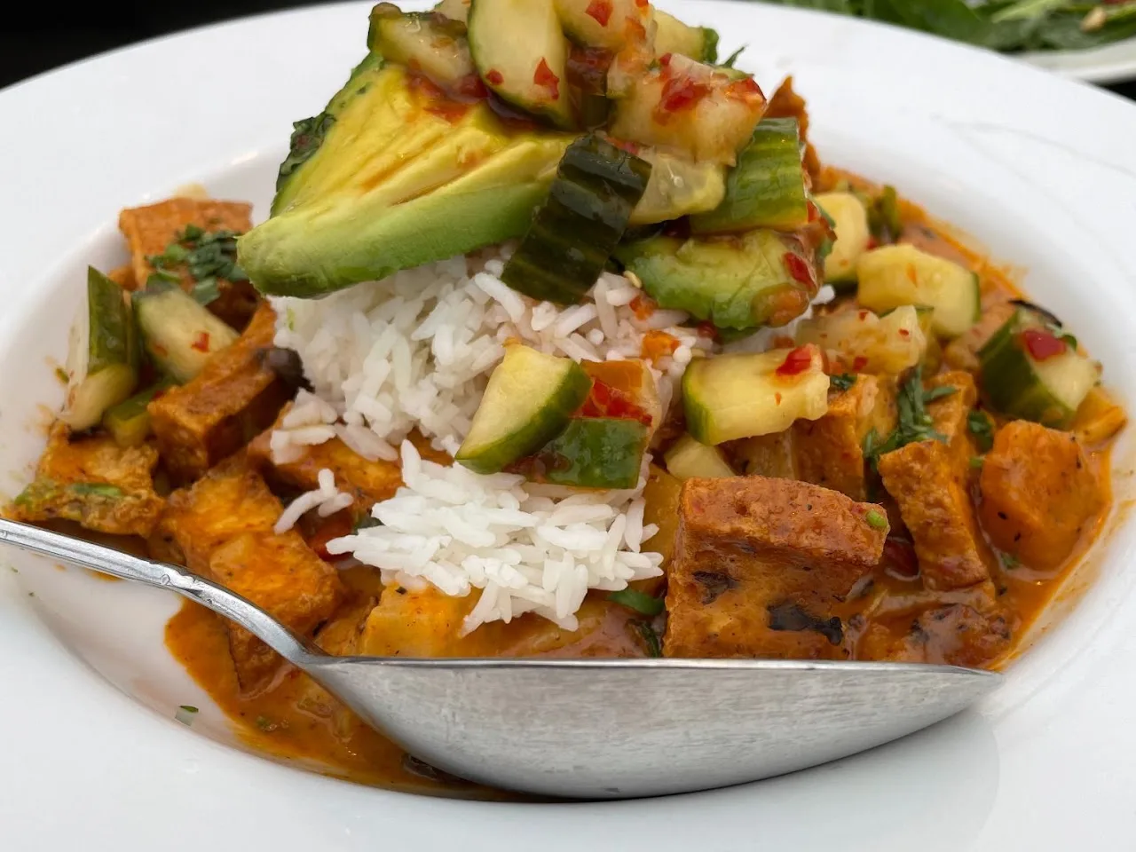 A colorful plate of rice, avocado, and spicy food